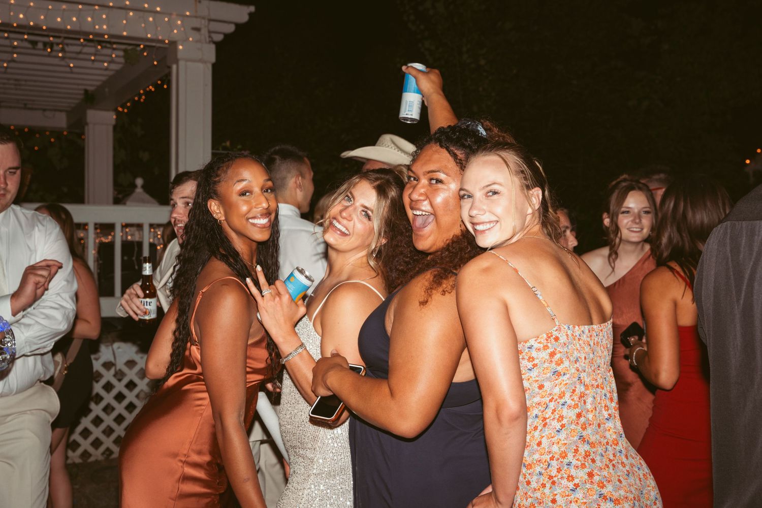 A group of party guests pose together at a nighttime celebration with drinks and smiles.