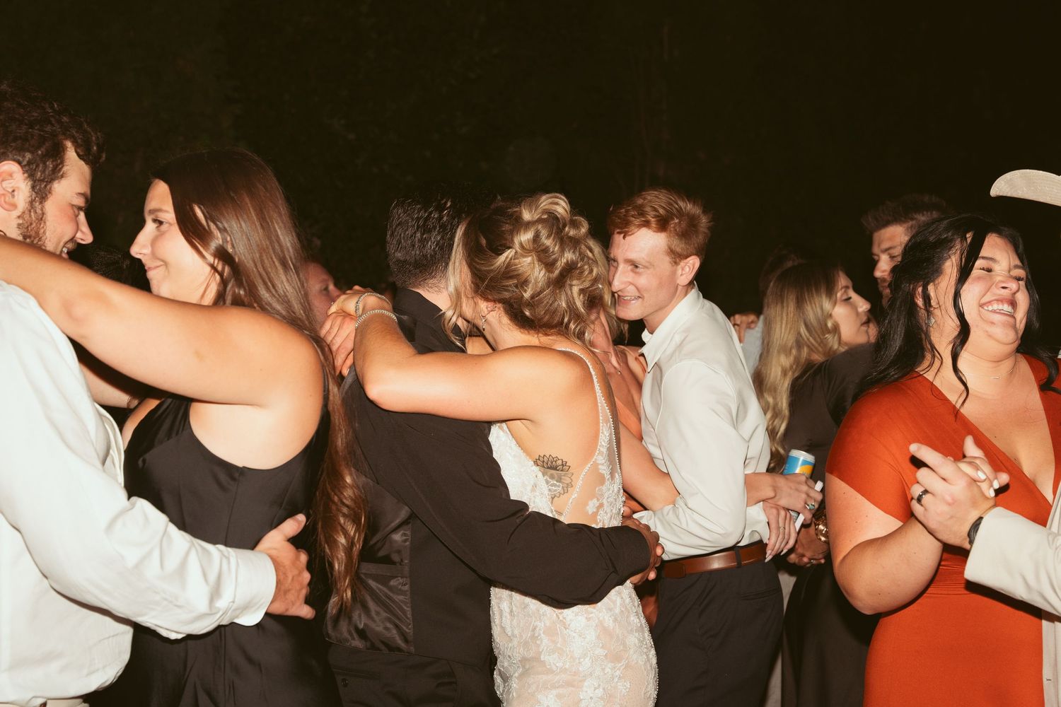 Wedding guests dancing in a conga line at an outdoor nighttime reception.