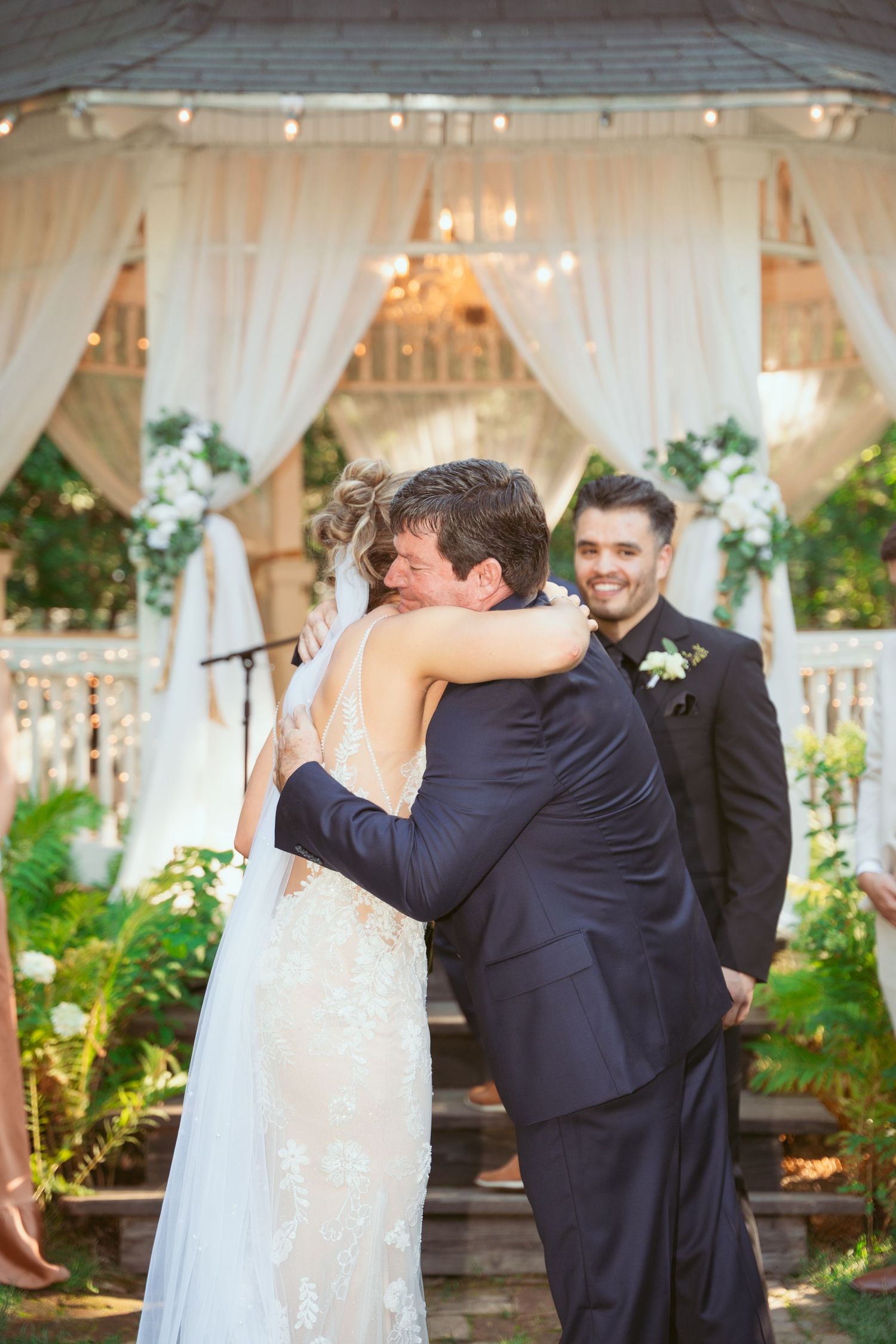 A tender moment captured during a wedding ceremony under an elegant white draped pavilion.