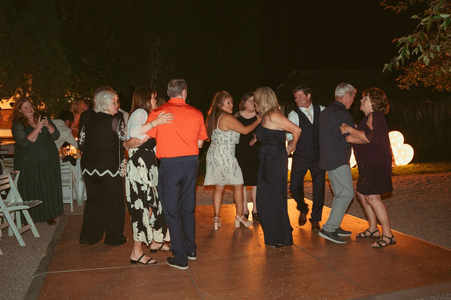 Wedding guests dancing together on an outdoor dance floor during an evening reception.