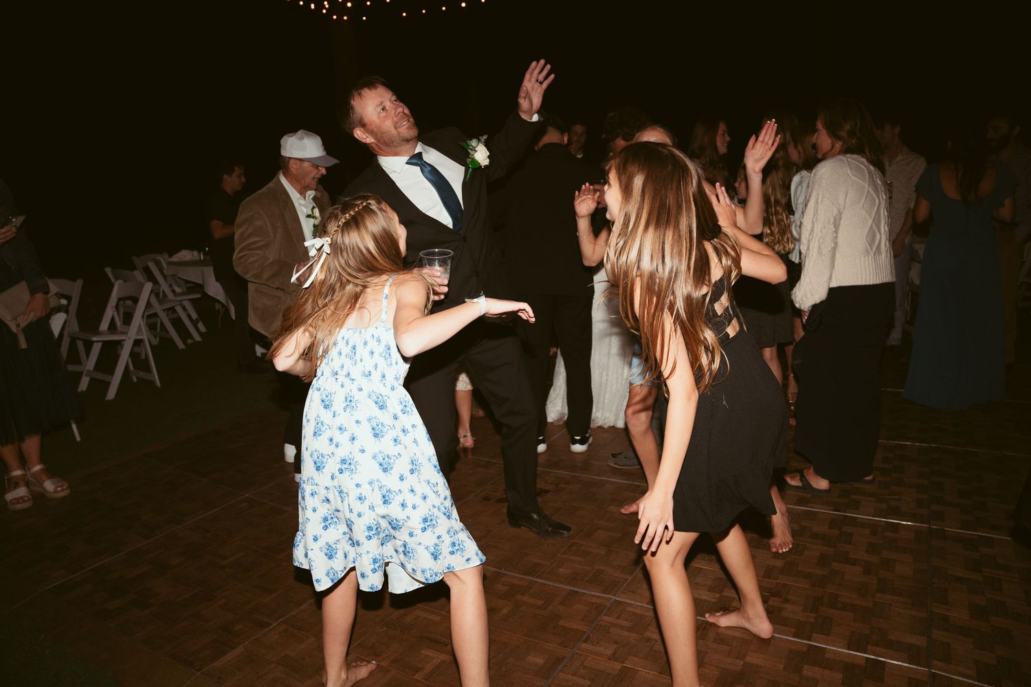 Guests dancing and celebrating at a nighttime outdoor wedding reception under string lights.