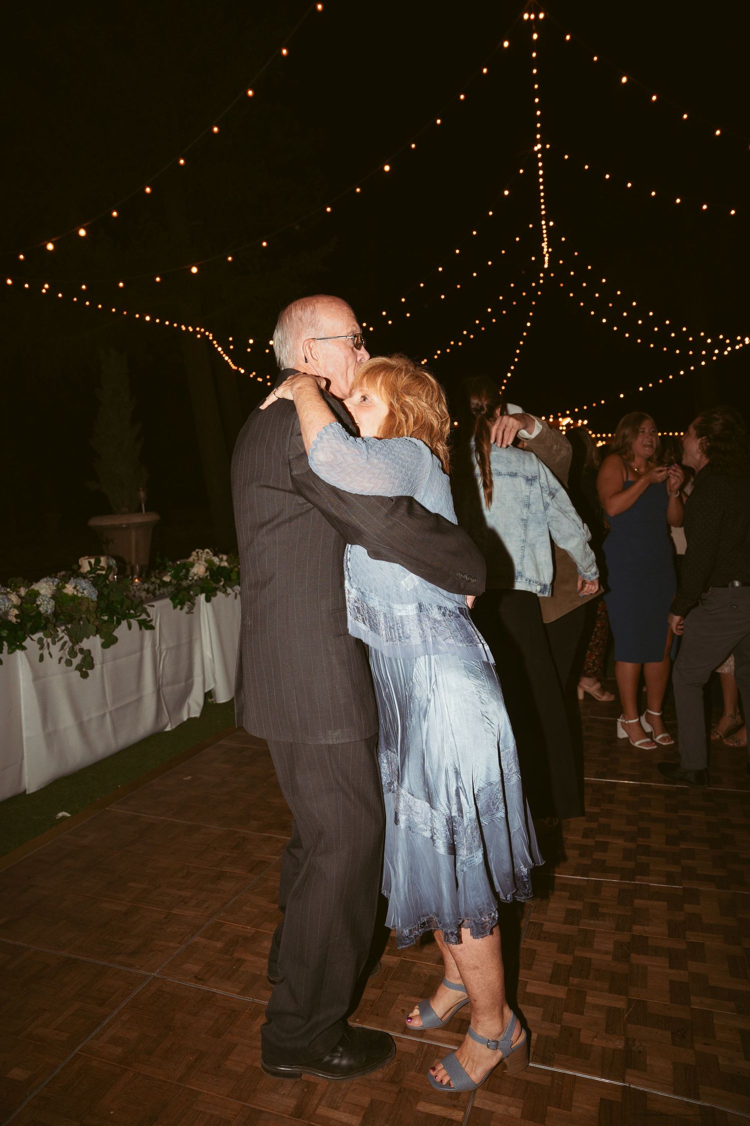 Couples dancing together under romantic string lights at an evening wedding reception on a brick patio.