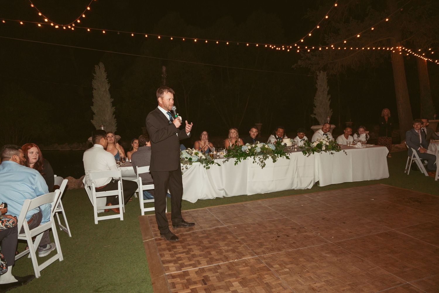 Wedding reception dance floor illuminated by string lights with guests enjoying the celebration.