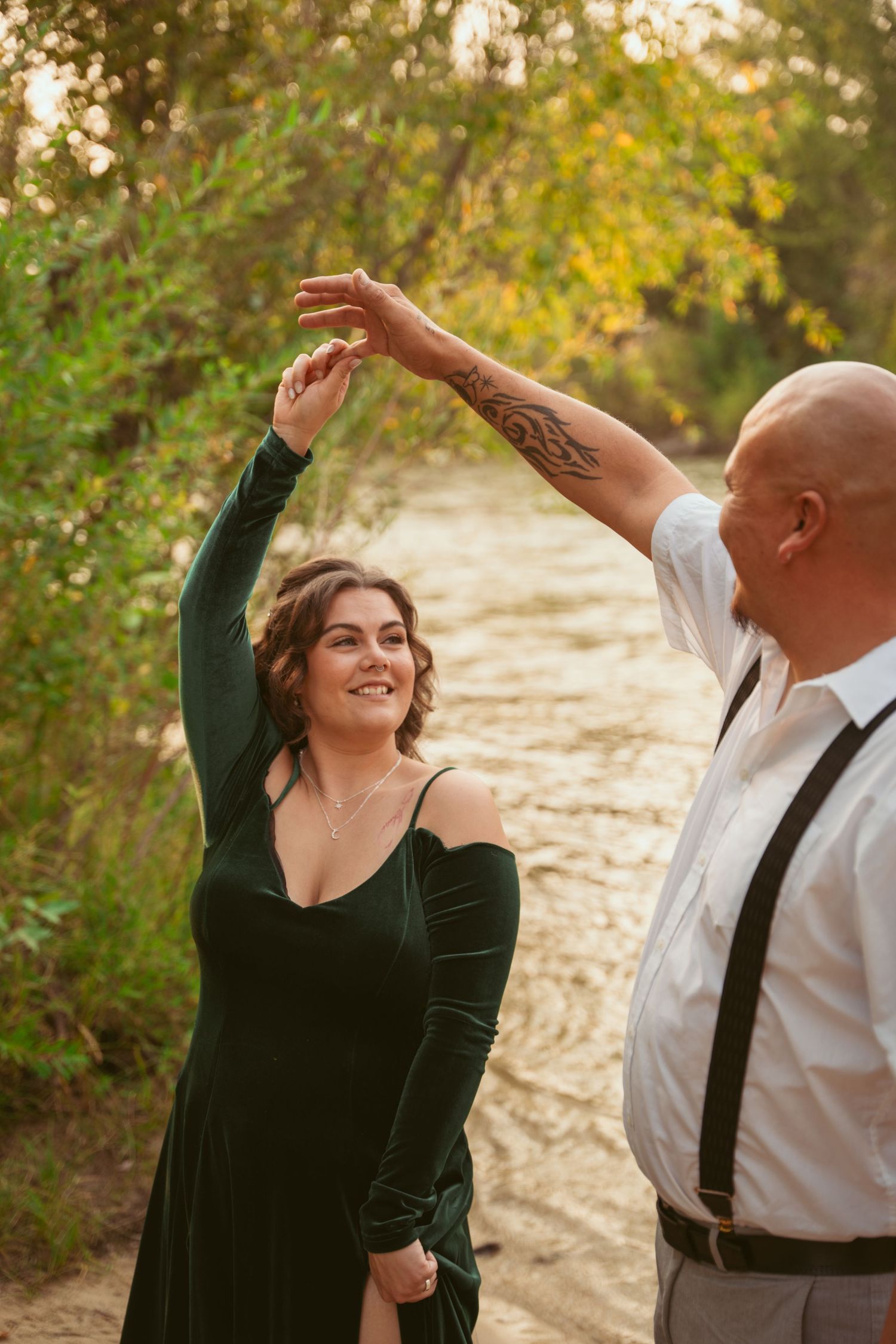 Dancing couple twirls together by a riverside during a golden autumn evening photoshoot.