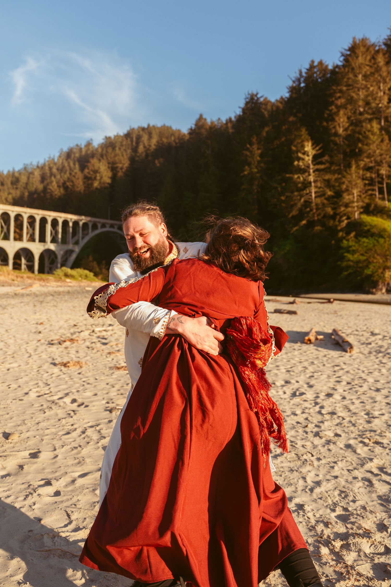 A joyful embrace on a beach with a historic bridge visible in the background.