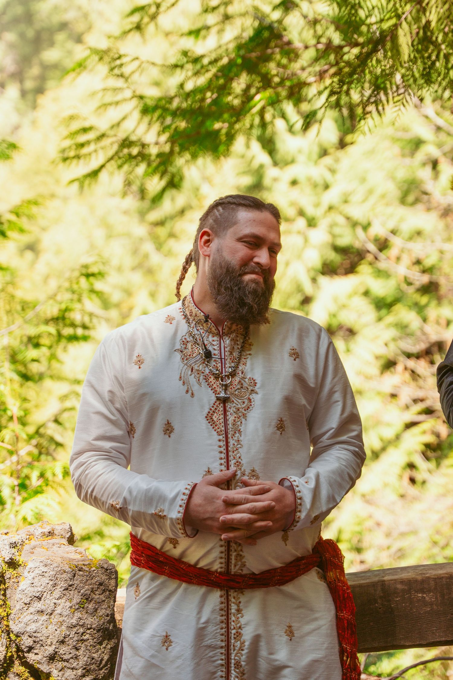 Person in ornate white medieval garb gestures during outdoor forest ceremony.