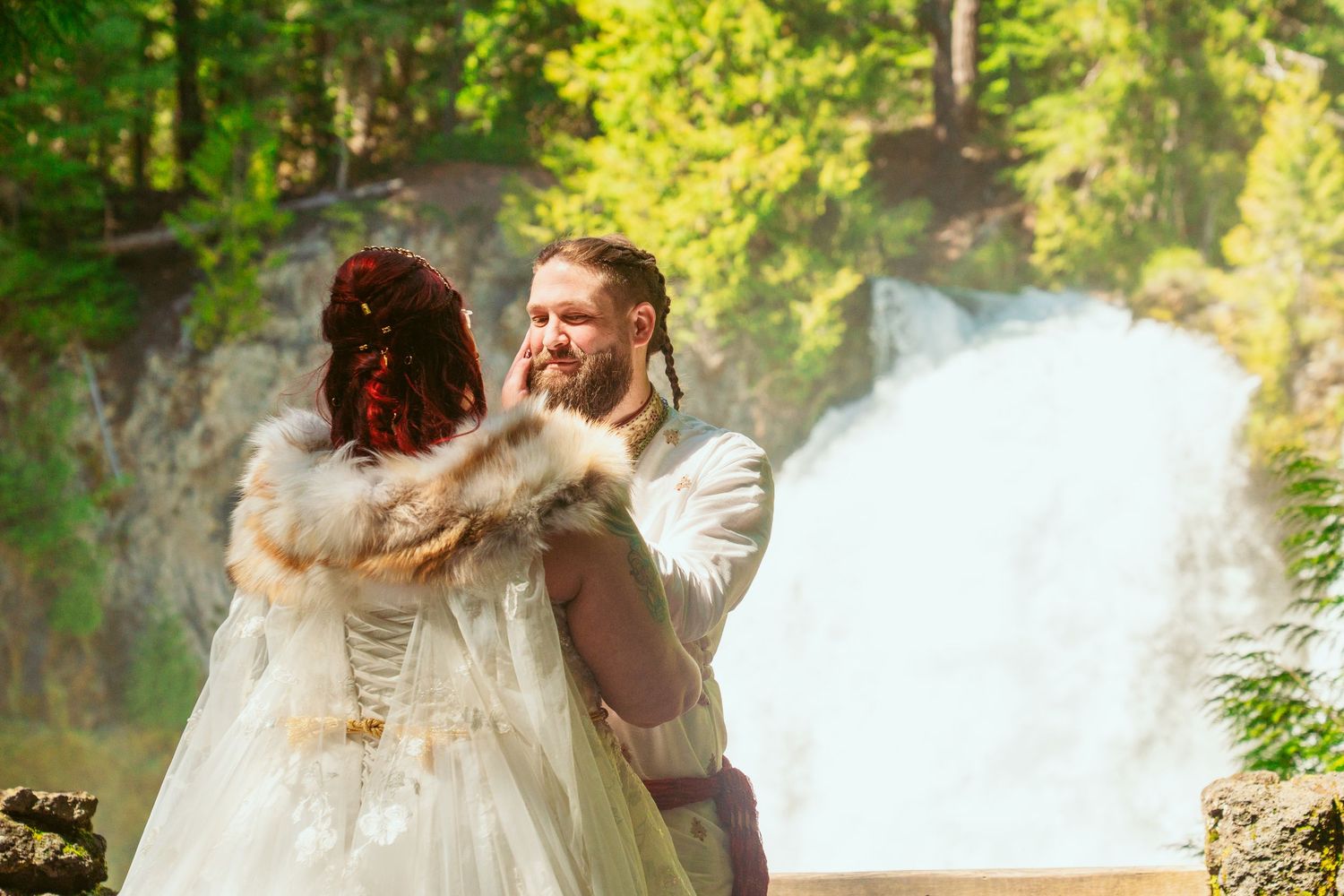 A couple shares an intimate moment during their wedding ceremony with a waterfall in the background.