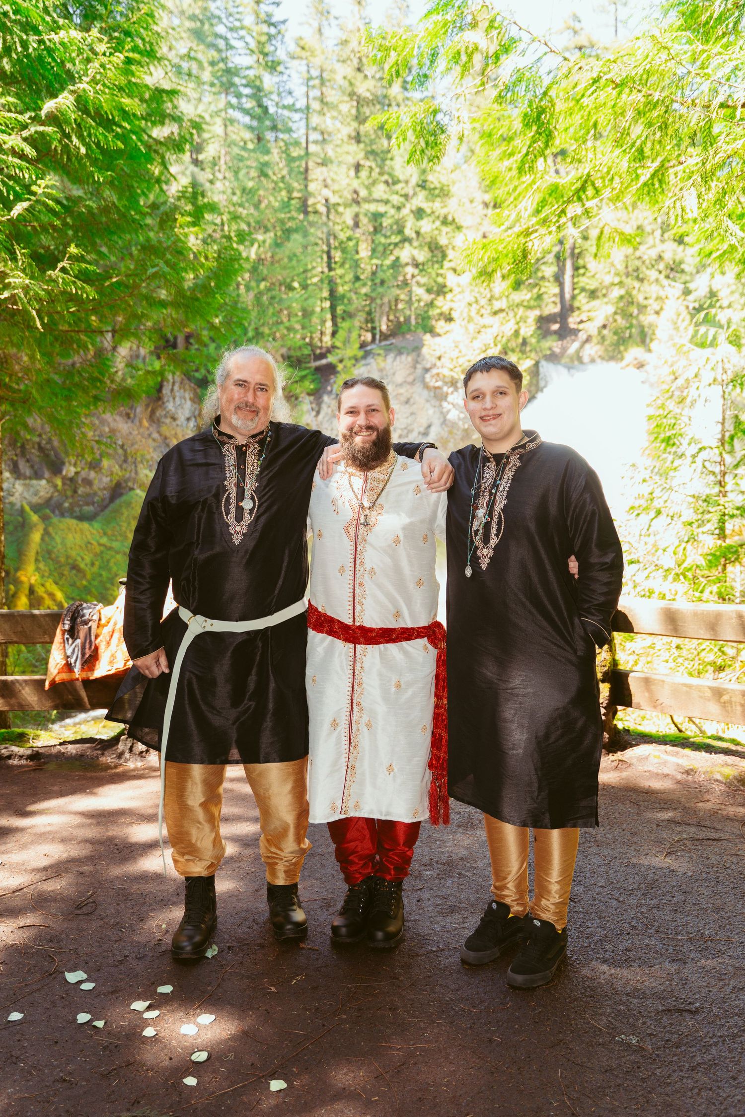 Wedding attendees in dark medieval costumes gather for photos in a wooded outdoor setting.