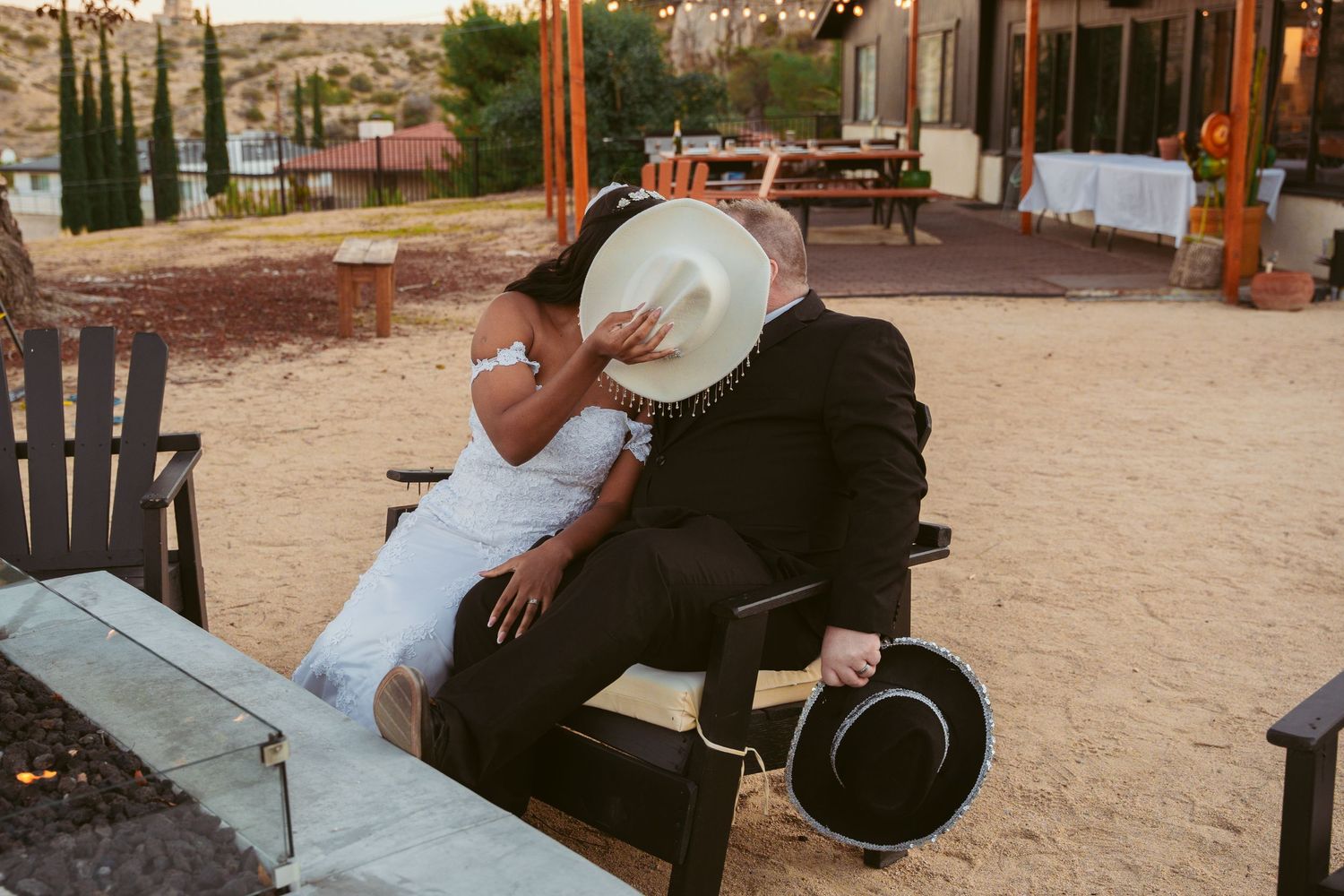 Couple posing for wedding photos in a sandy desert setting with rustic wooden structures.