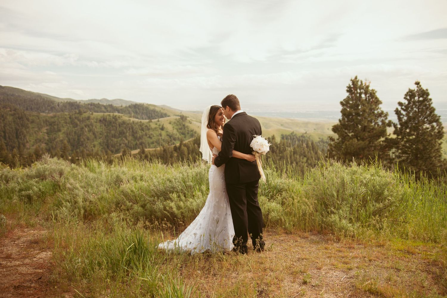 A couple shares romantic moments on a hilltop with mountain views in the background.