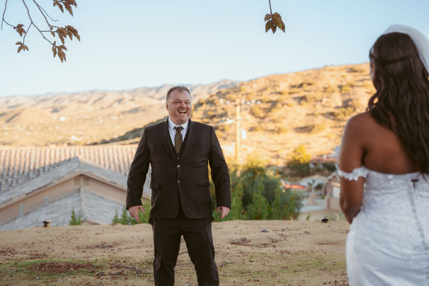 A wedding couple shares a playful moment in a desert landscape at sunset.