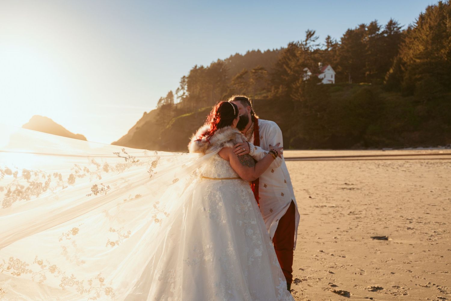 A couple dances together on a scenic beach at sunset with mountains and trees in the background.
