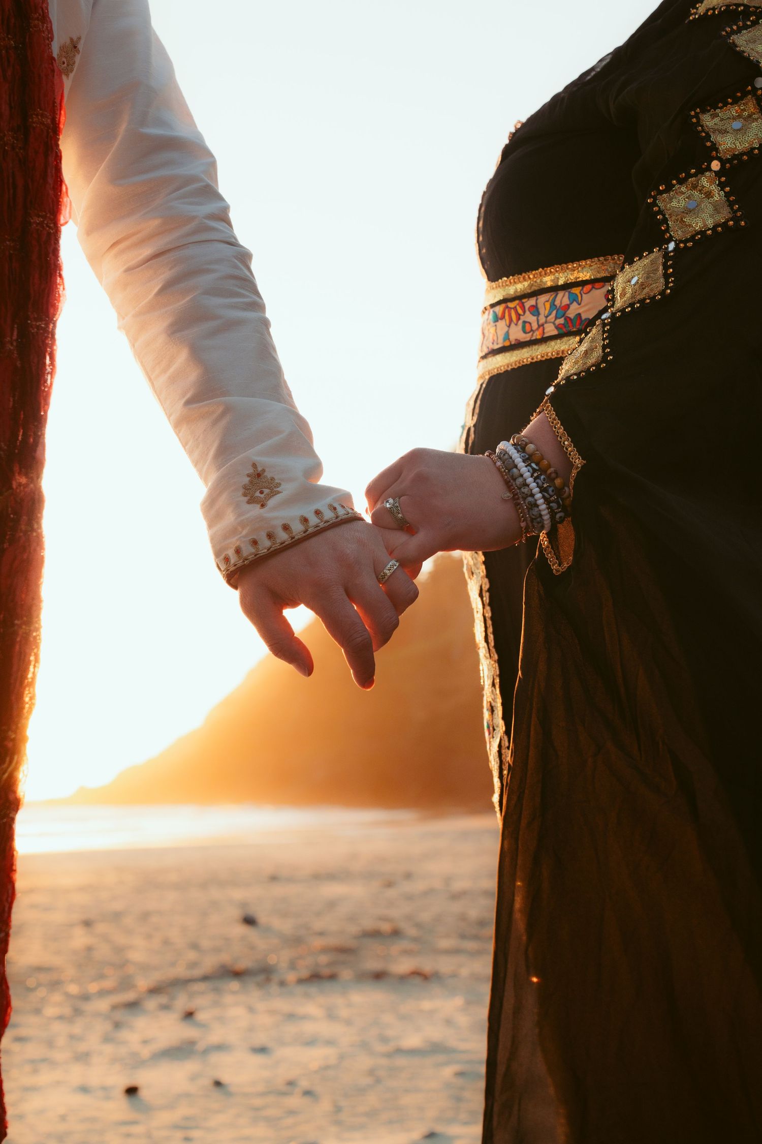 Close-up of couple holding hands against sunset beach backdrop.