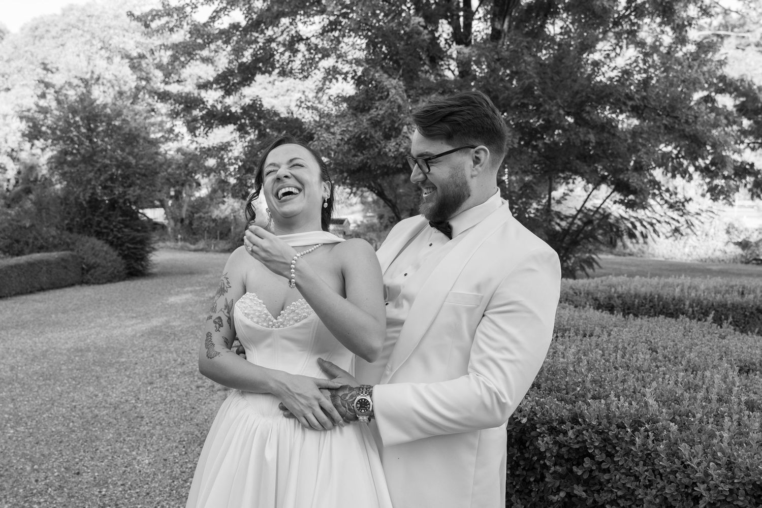 A black and white photo captures a couple sharing a genuine laugh during their wedding photoshoot.