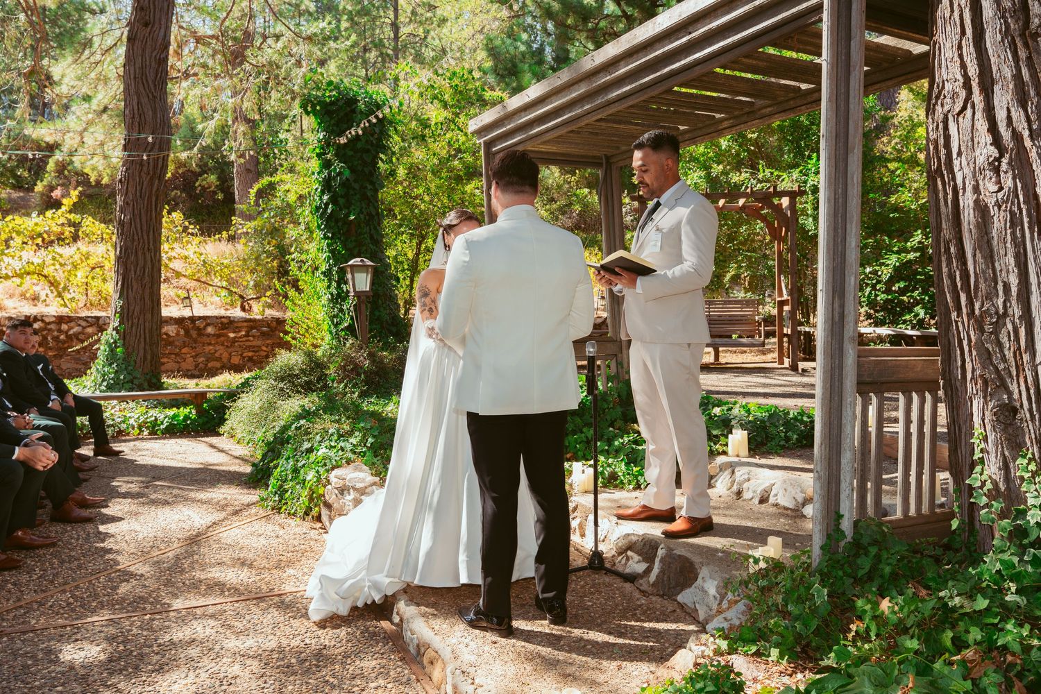 Outdoor wedding ceremony setup with wooden pergola and natural garden surroundings.