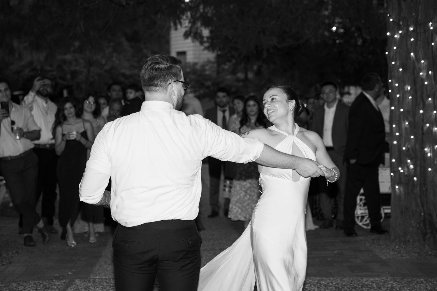 A couple performs a lively dance move during their wedding reception under twinkling lights.
