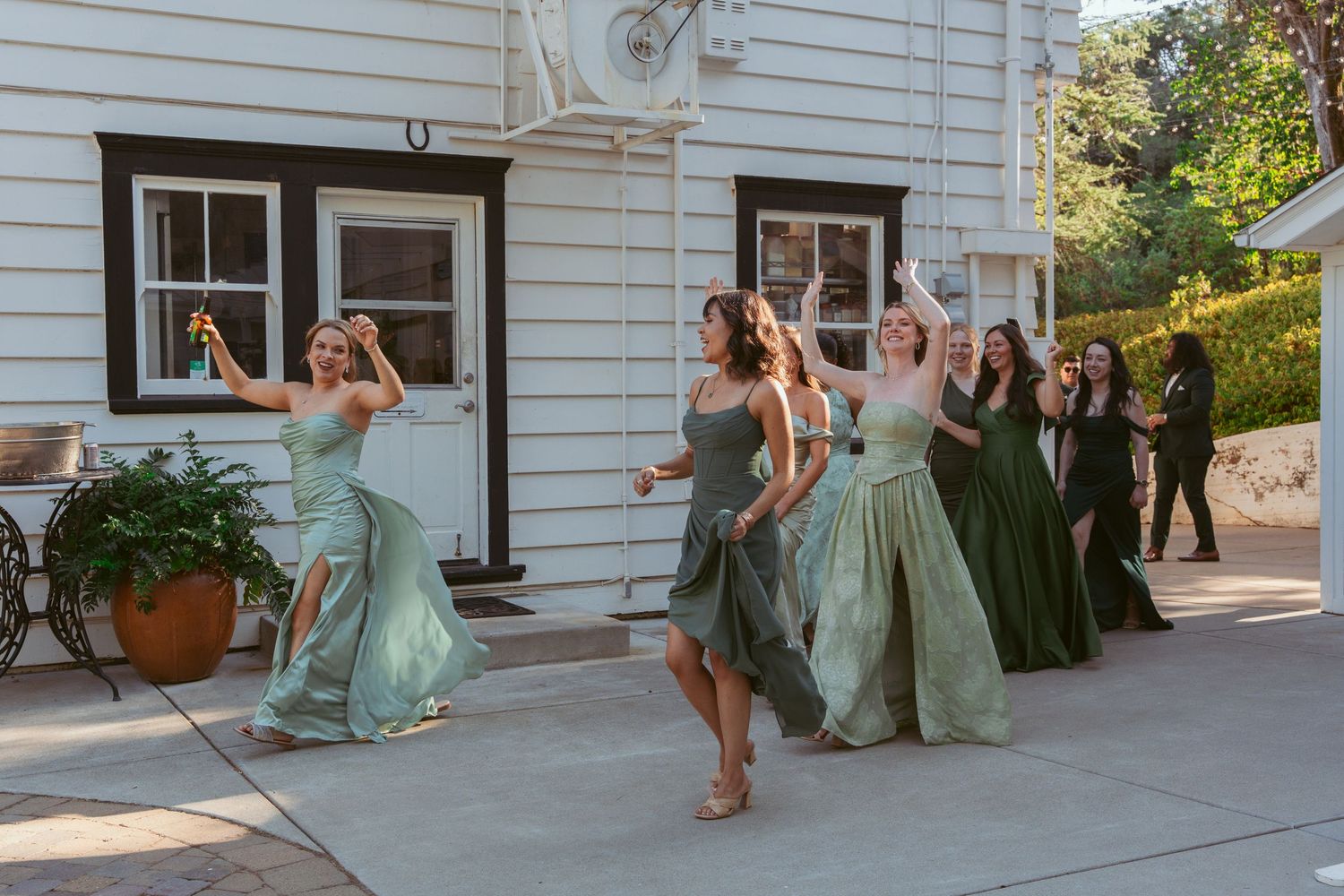 Wedding party members in coordinated dresses performing choreographed moves outside.