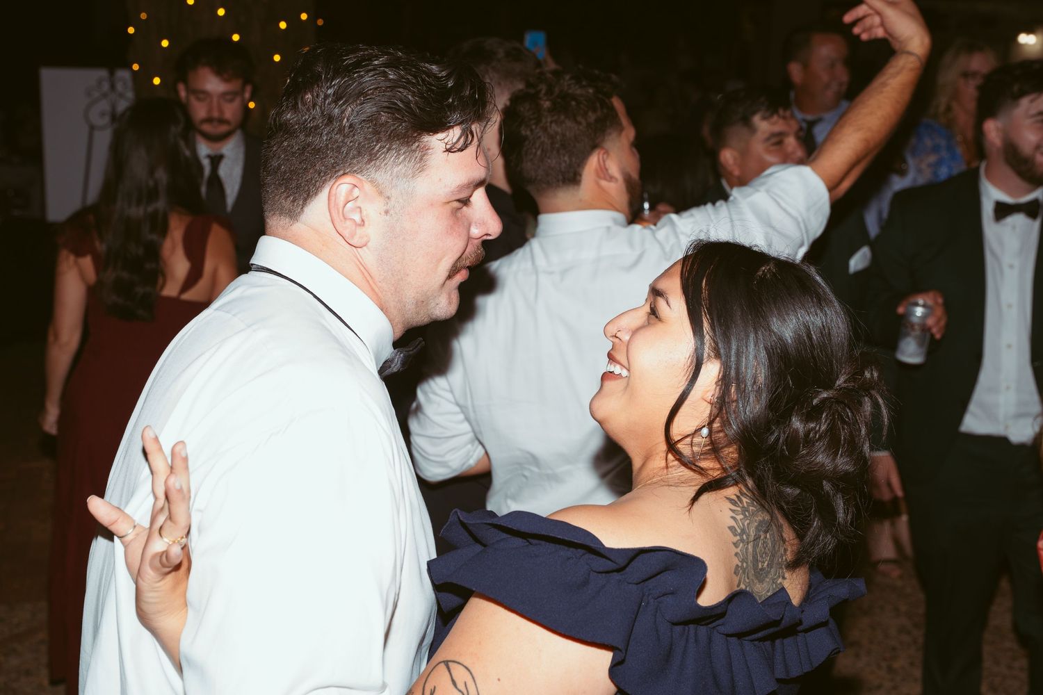 Wedding guests dance and celebrate at an evening reception under string lights.