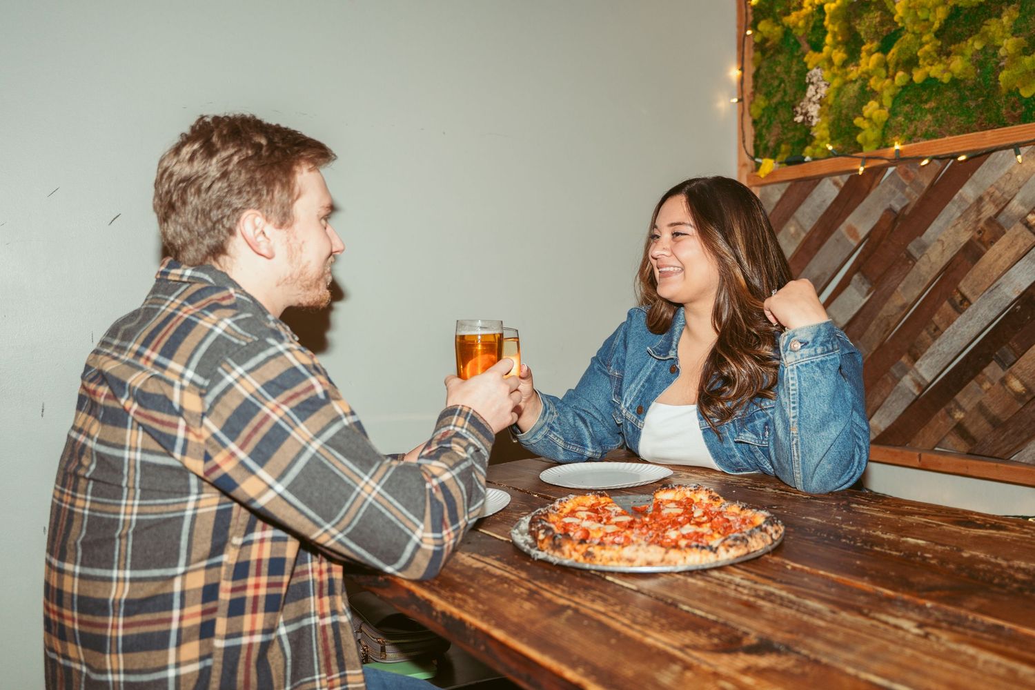 Candid moment of friends laughing while sharing pizza and drinks at a restaurant.