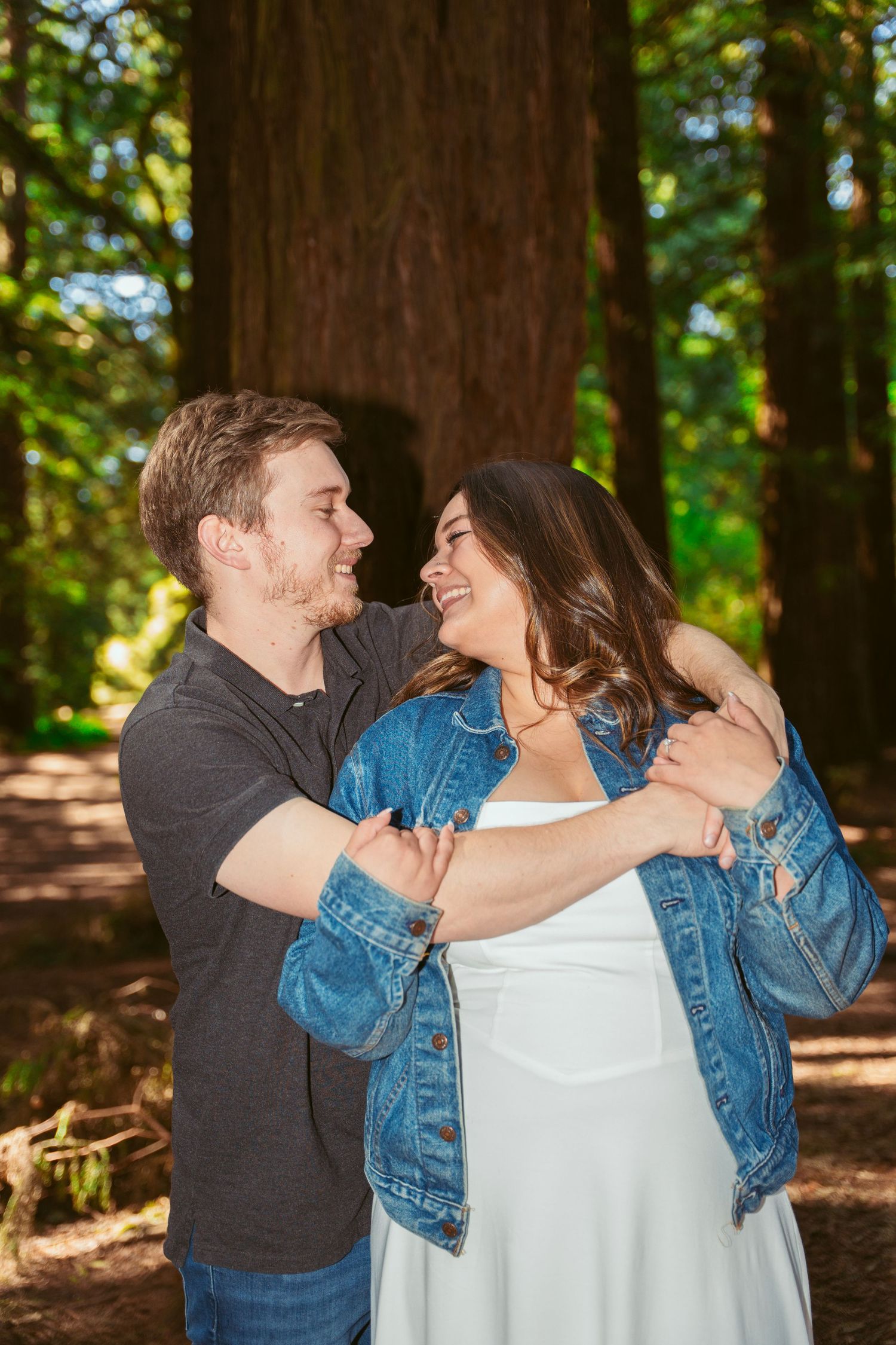 A couple shares a loving embrace while sitting together in a sunny forest setting.