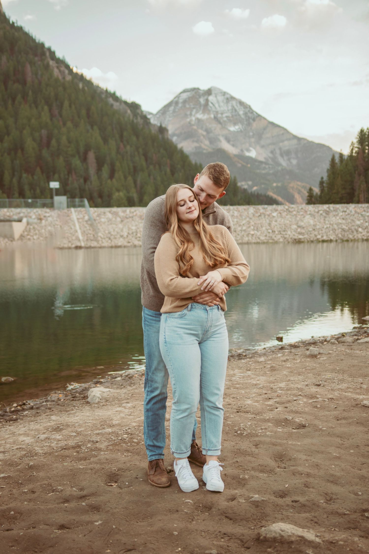 Couple in casual wear sharing intimate moments by a mountain lake with scenic views.