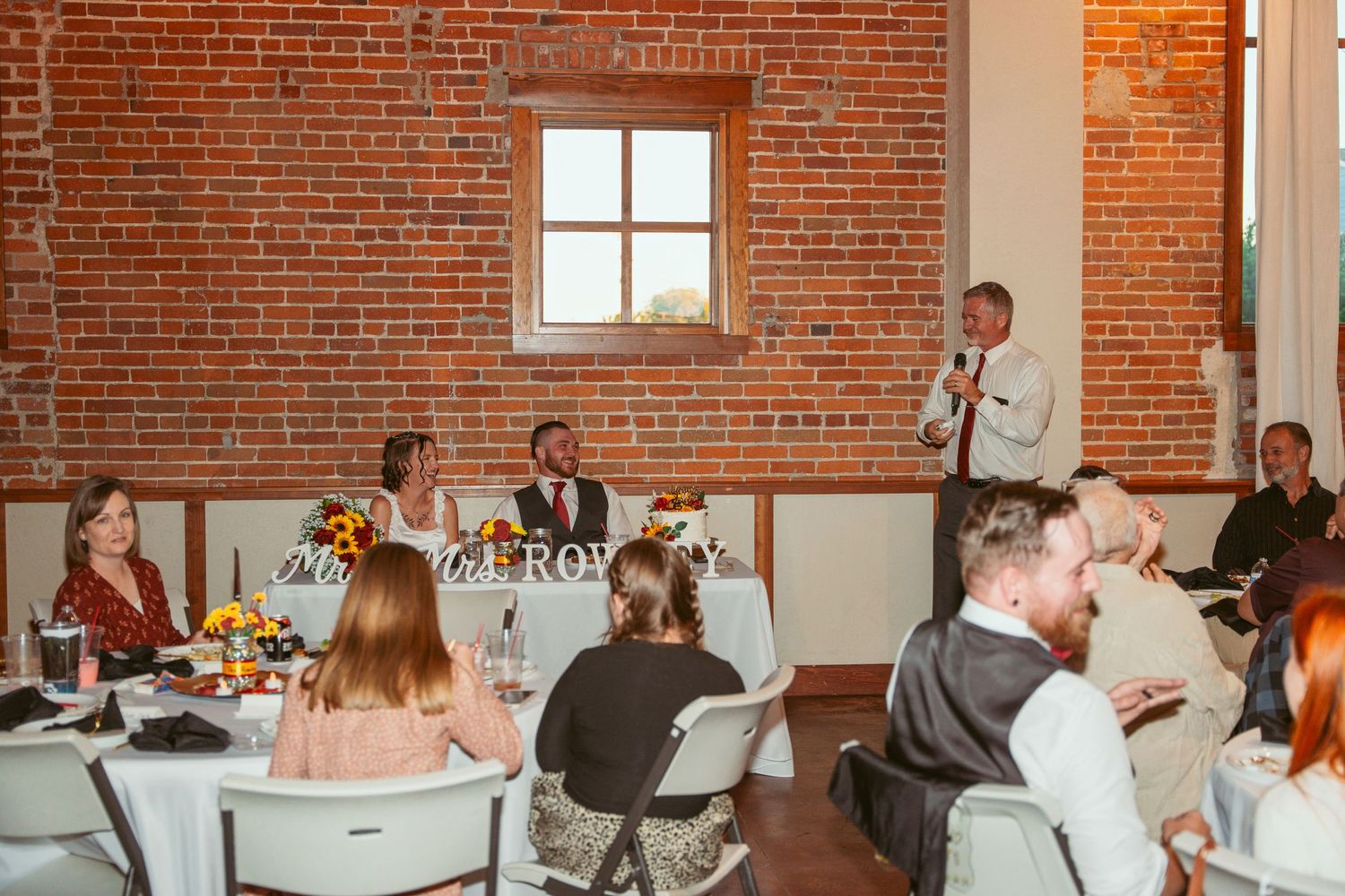 Wedding celebration in a rustic brick-walled venue with tables and festive decorations.