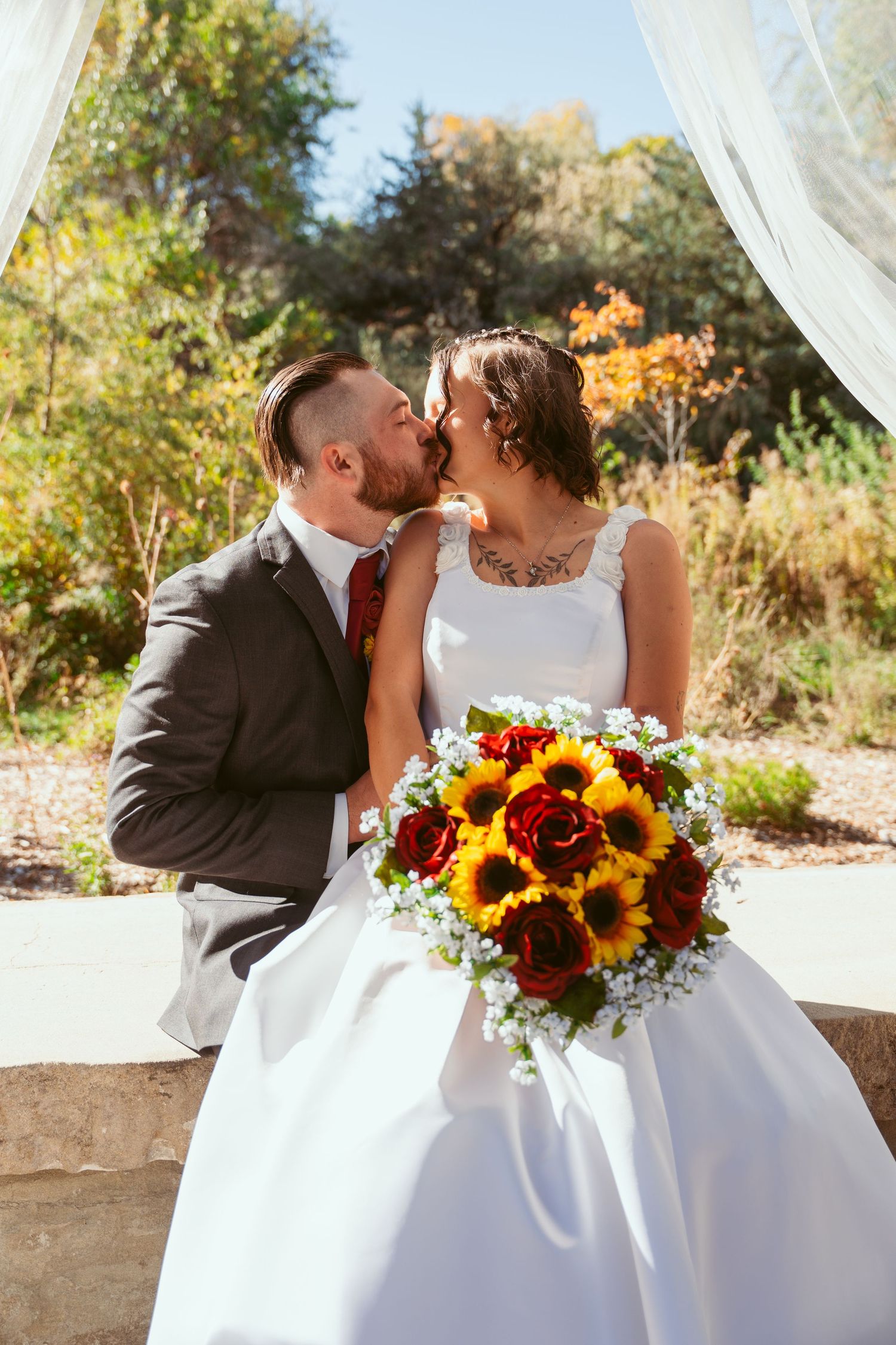 Romantic wedding couple shares intimate moments under pavilion with sunflower bouquet.