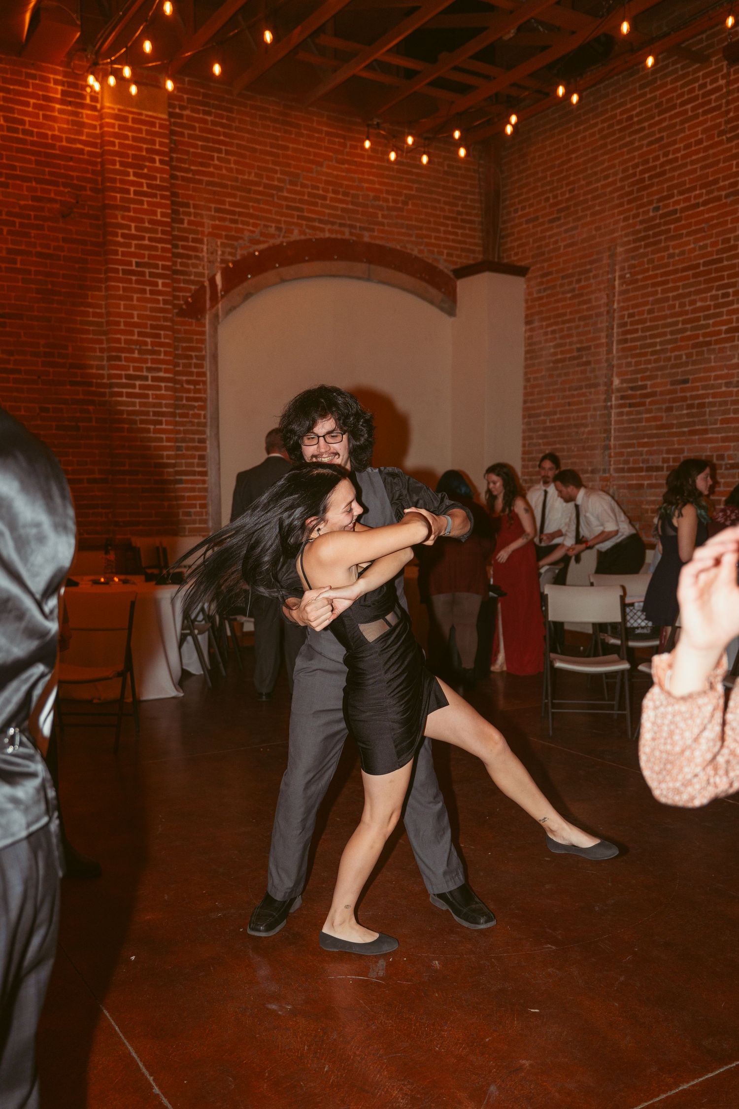 Dancers performing dramatic dips and spins on the dance floor of a brick-walled venue.