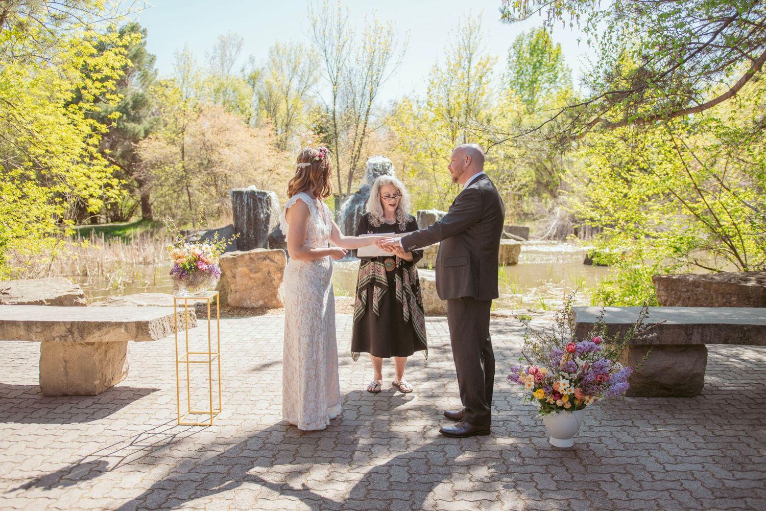 Wedding ceremony setup with wooden chairs and floral arrangements on a sunny outdoor patio.