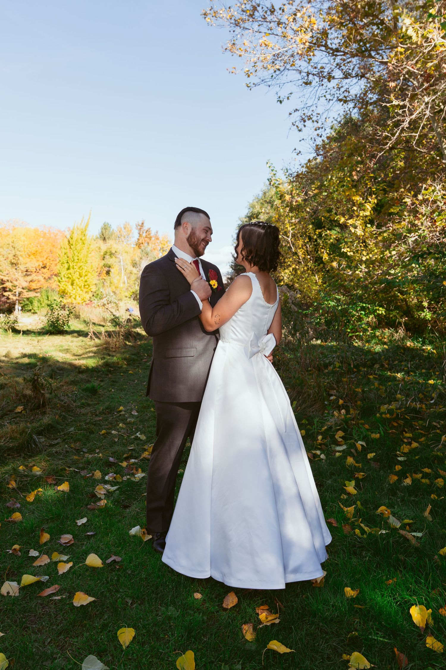 A romantic wedding couple embraces on an autumn day with fallen leaves scattered on the ground.