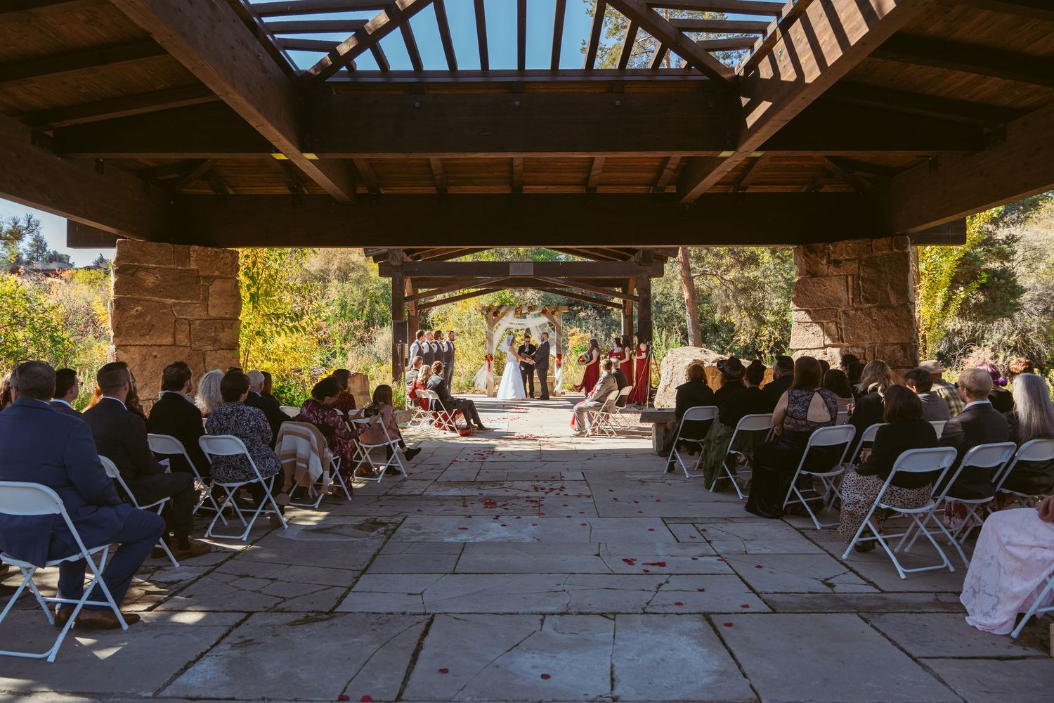 Wide-angle view of empty white chairs arranged under a covered stone pavilion.