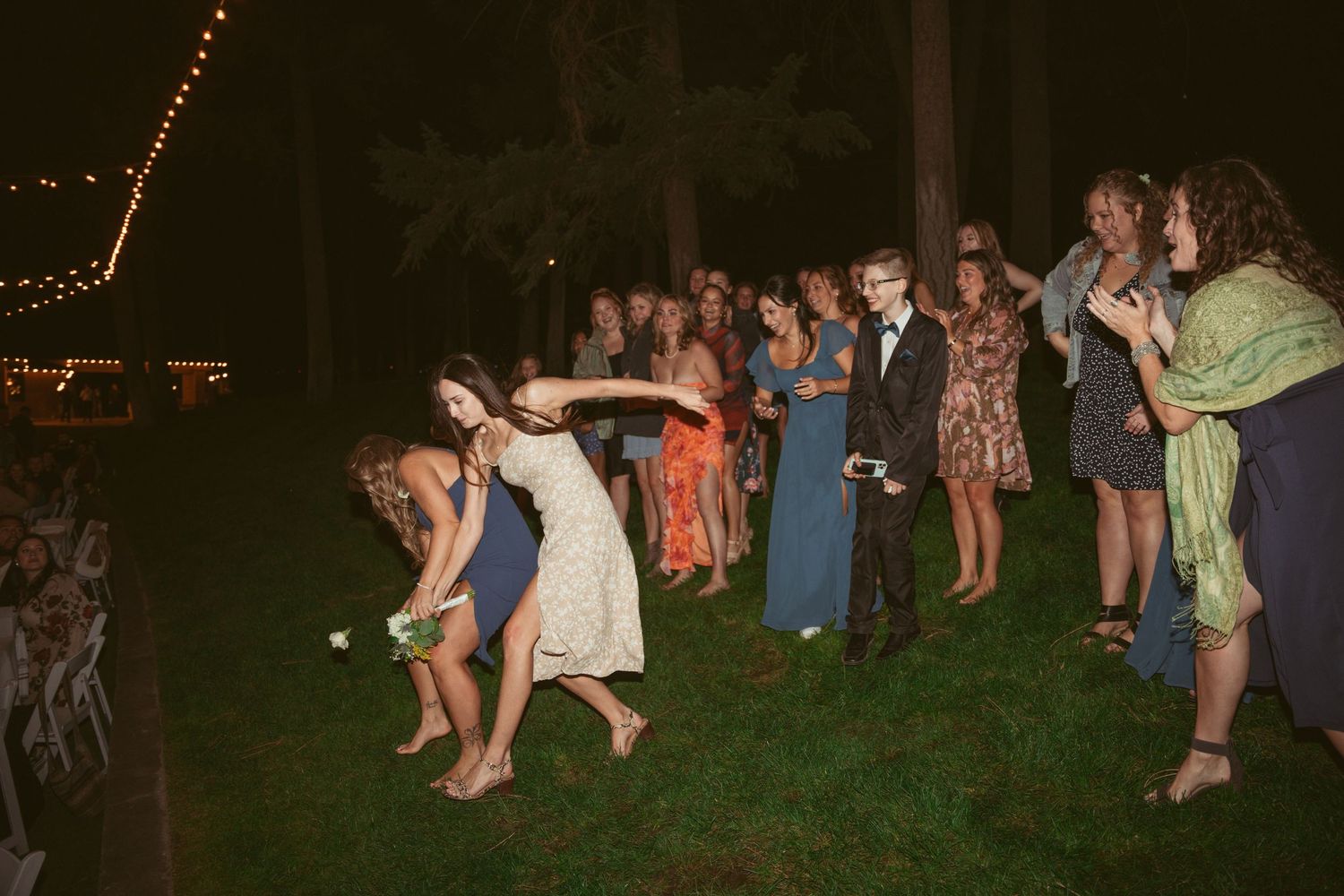 Wedding guests dance in groups on an outdoor patio during an evening reception.