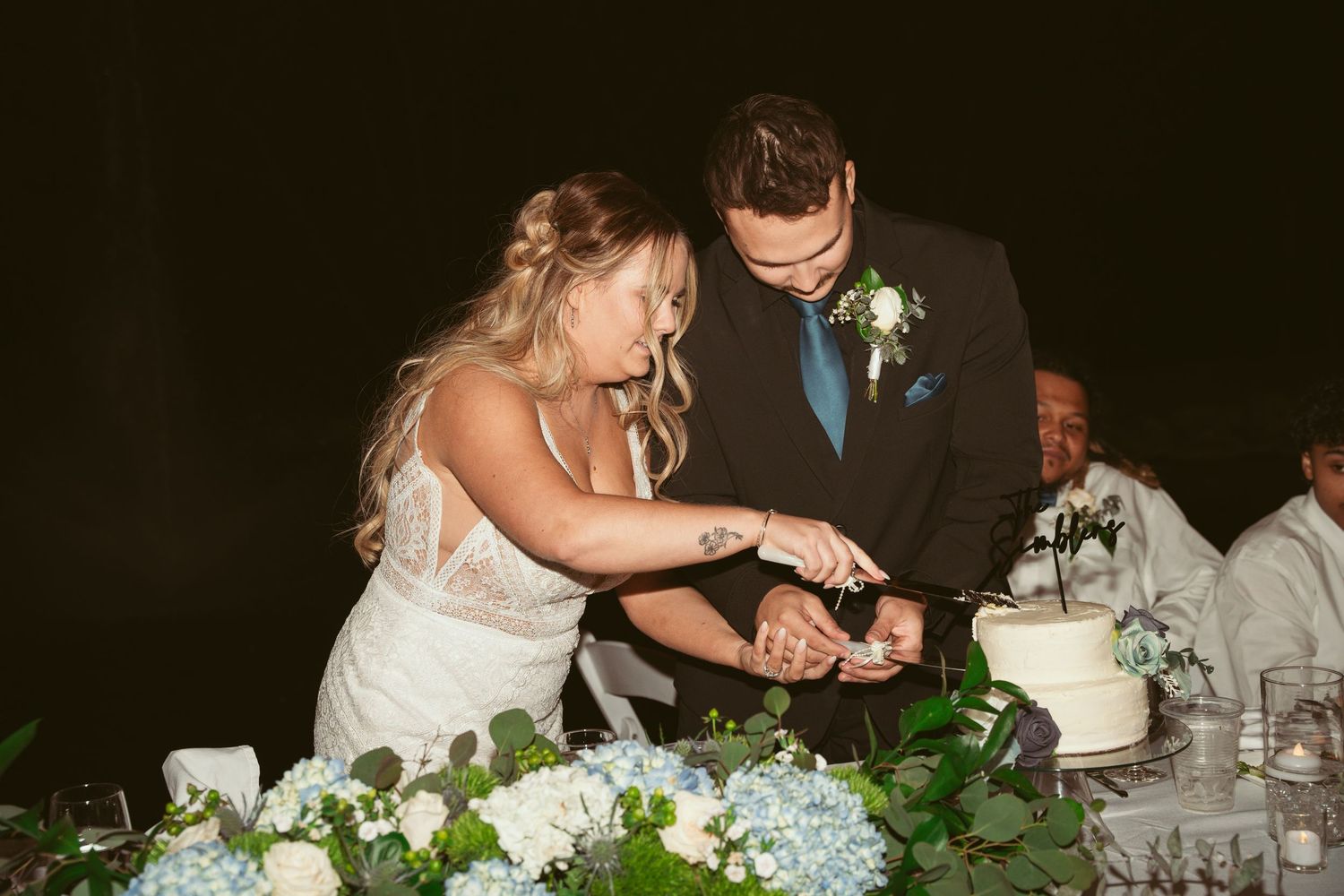 Couple cuts their wedding cake together at an elegant reception with floral table decorations.