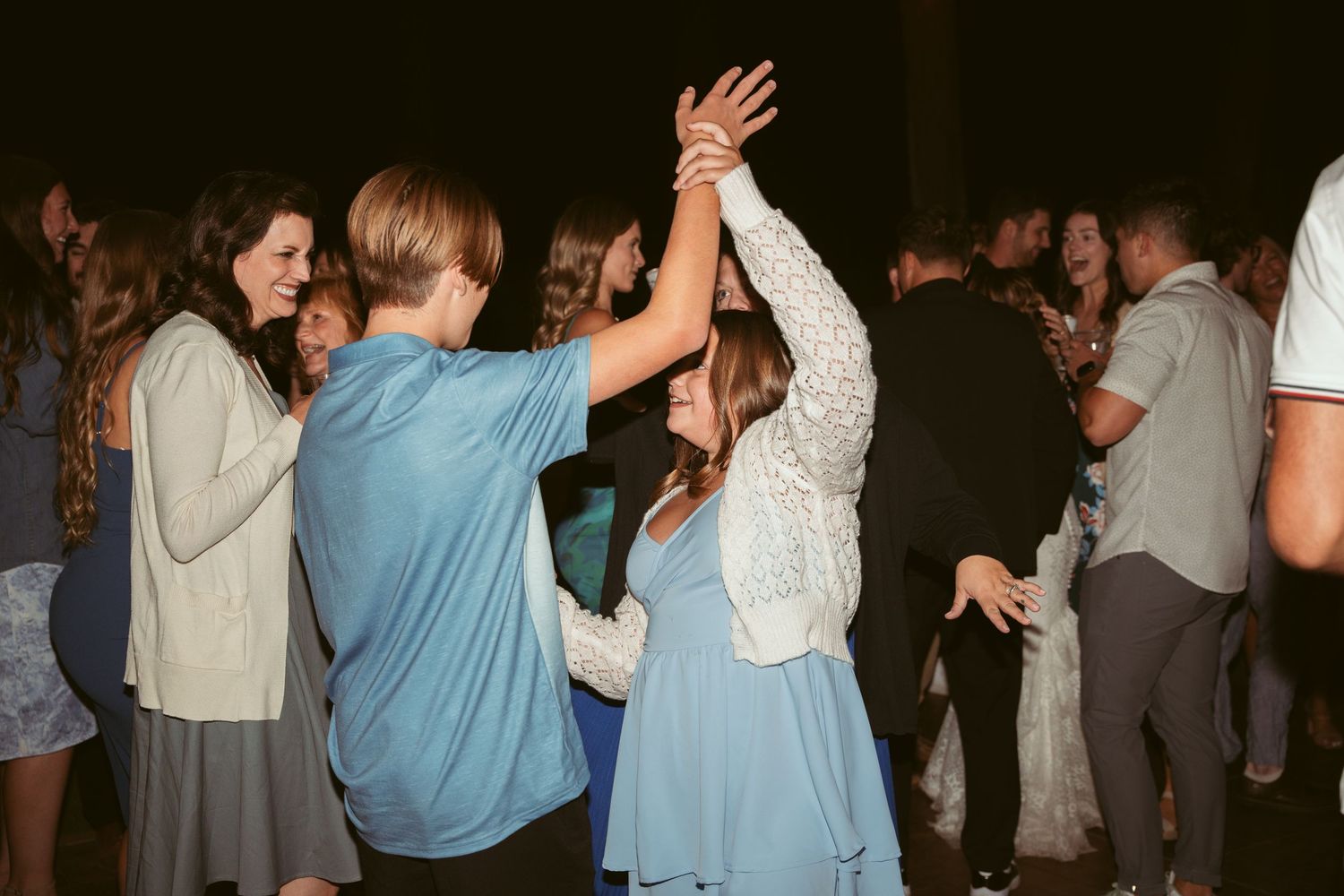 People dancing and raising their hands during a festive outdoor wedding reception.