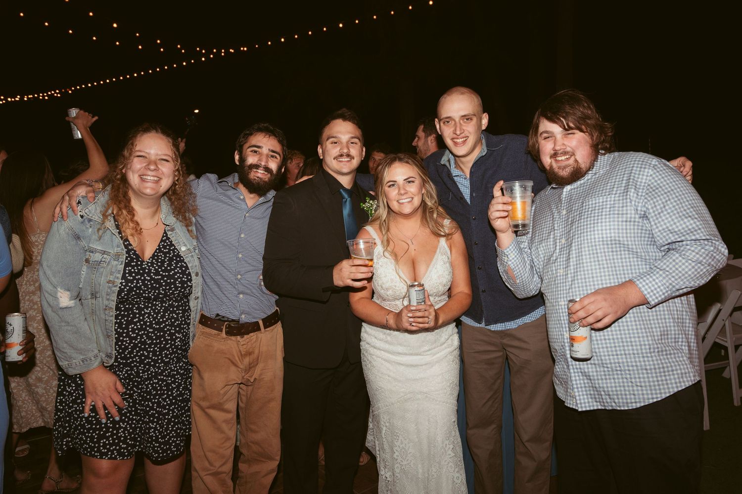 Guests celebrating at a nighttime wedding reception with string lights overhead and a festive atmosphere.