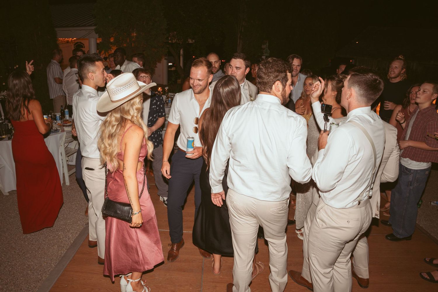 Wedding guests dancing and celebrating on an illuminated outdoor dance floor at night.