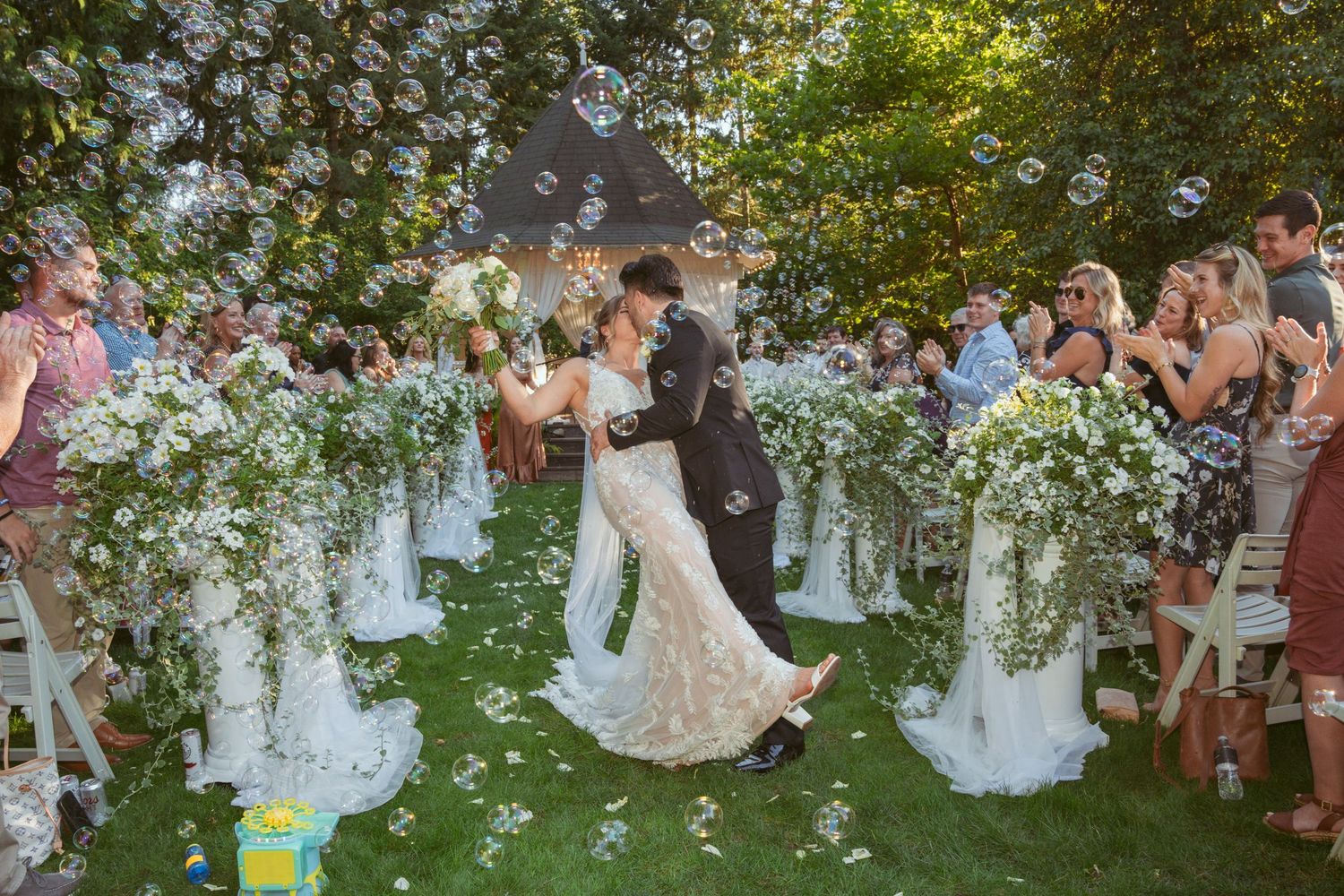 Wedding guests dance together on a lawn during an outdoor celebration at sunset.