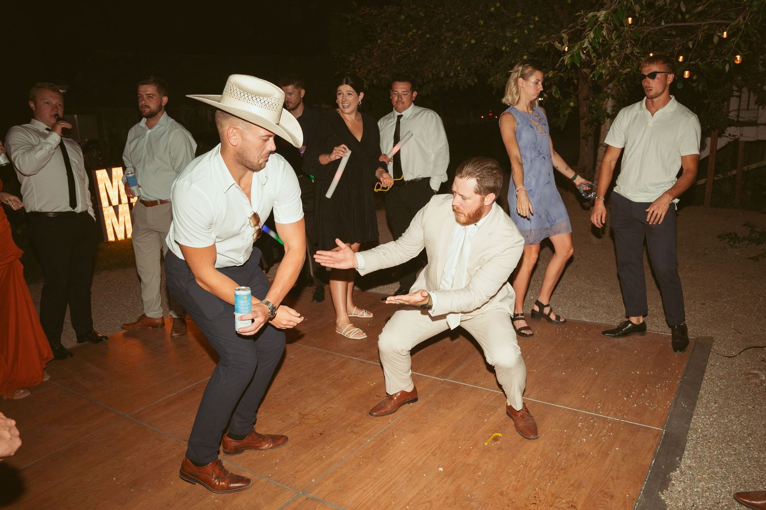 Wedding party members dancing and celebrating on an outdoor dance floor.