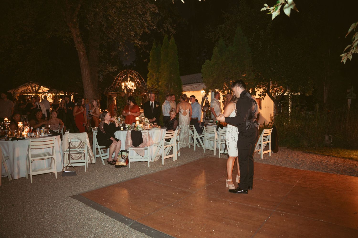 Outdoor wedding reception venue with white chairs and string lights at night.