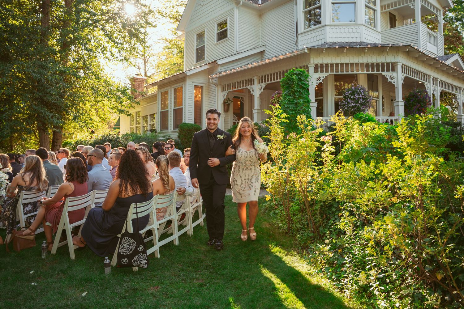 Elegant Victorian-style house serves as backdrop for outdoor wedding with guests seated on the lawn.