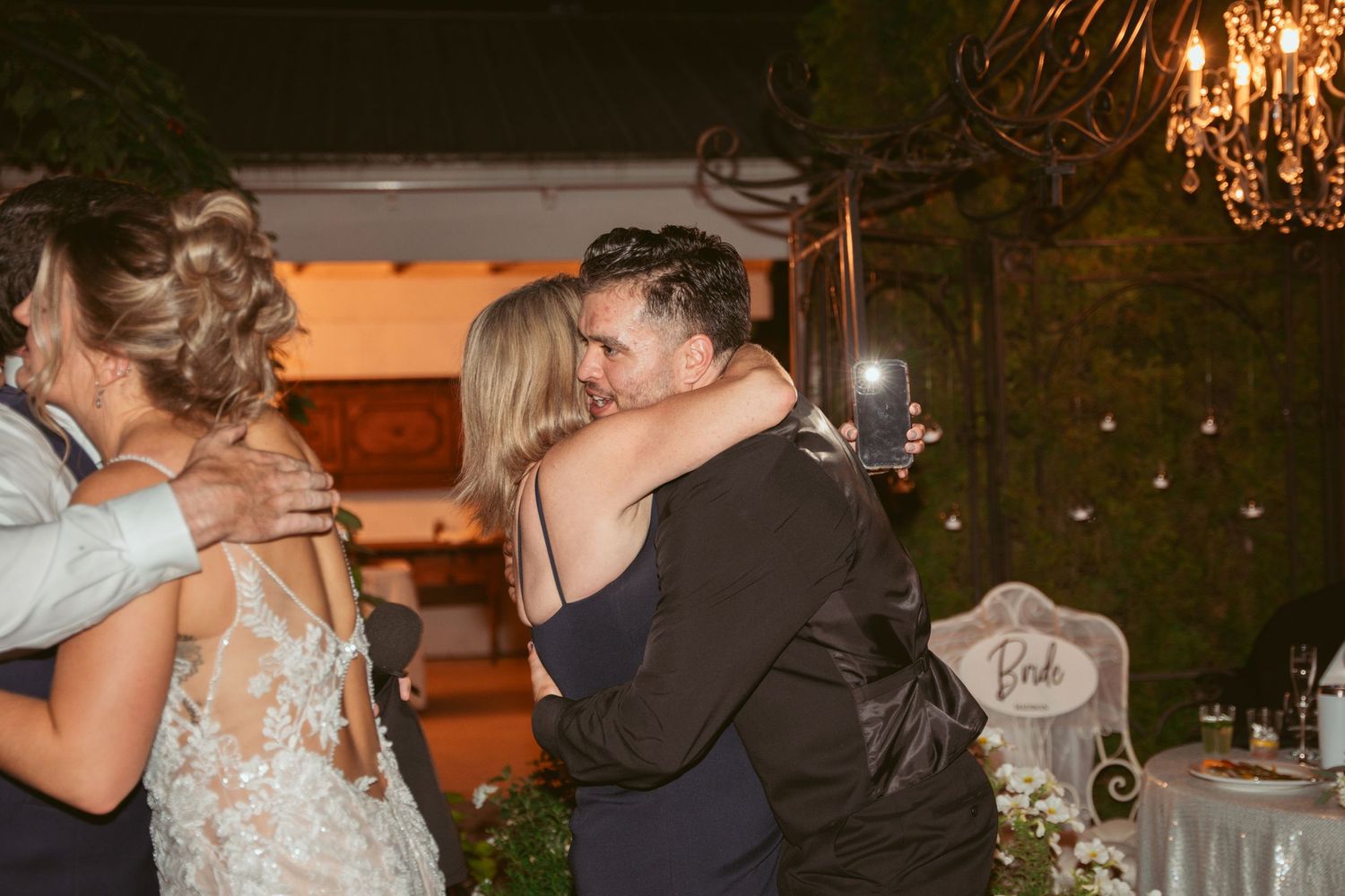 Wedding guests dancing and celebrating at an outdoor evening reception under elegant chandeliers.