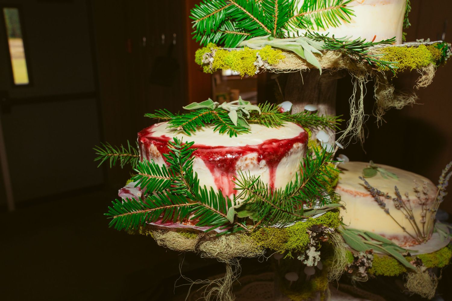 Elegant wedding cake decorated with pine branches and red accents in a woodland theme.