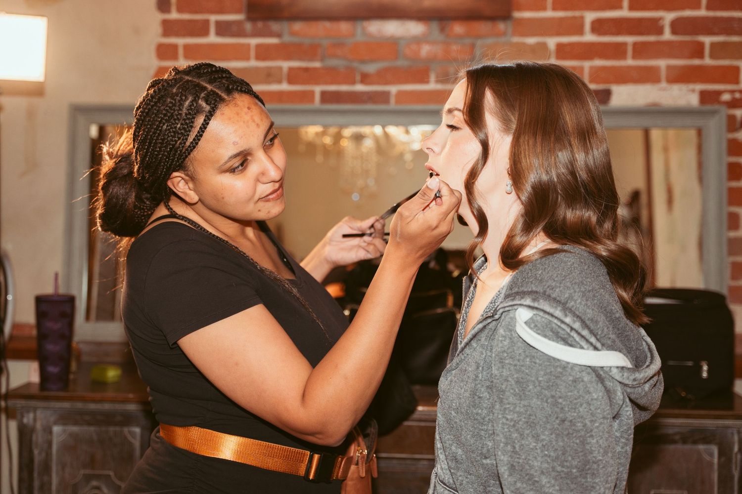 Close-up of makeup application in progress against a warm brick backdrop.