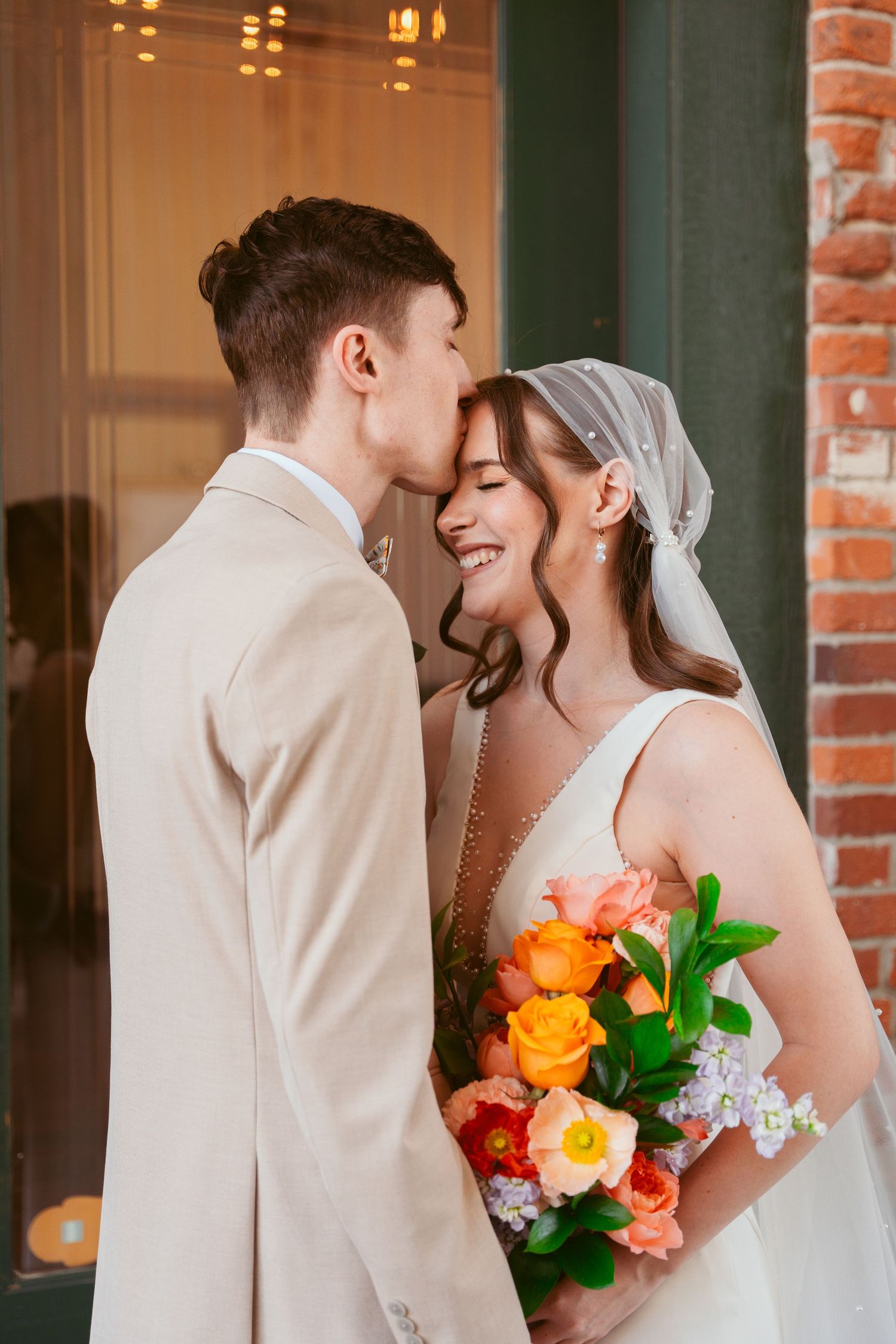 An intimate wedding portrait showing a sweet moment with colorful flowers and a beige suit.