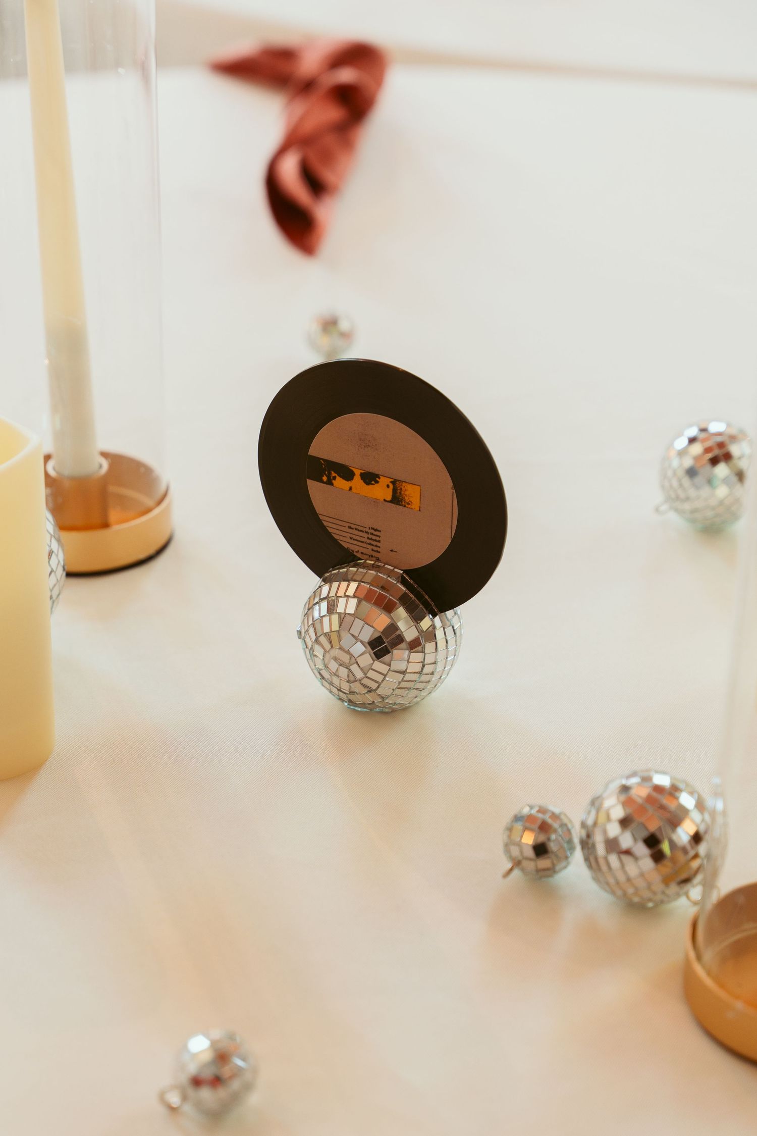 Minimalist table decor with white candles and mirrored disco ball ornaments.