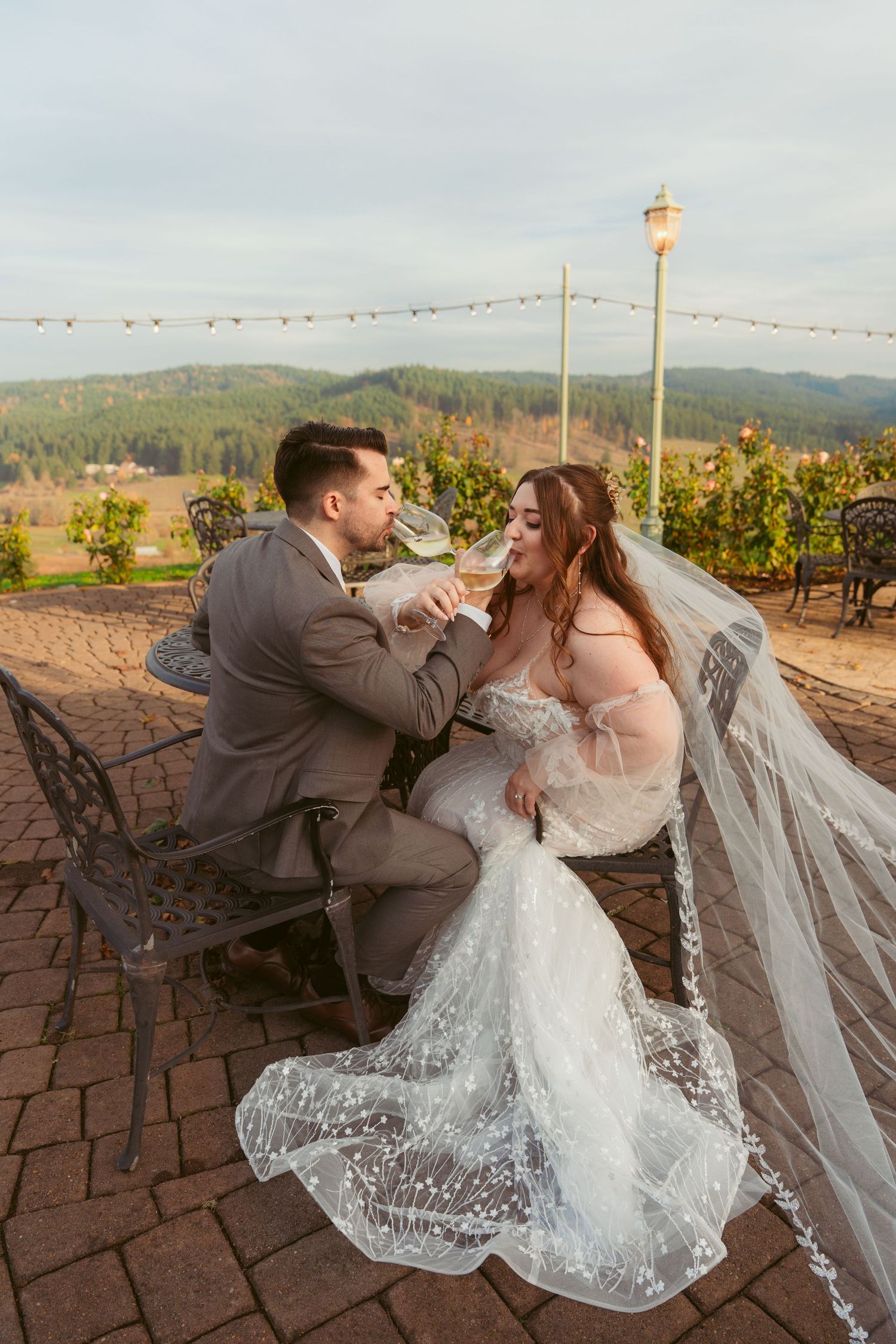 Couple shares romantic wine toast on brick patio with vineyard views.