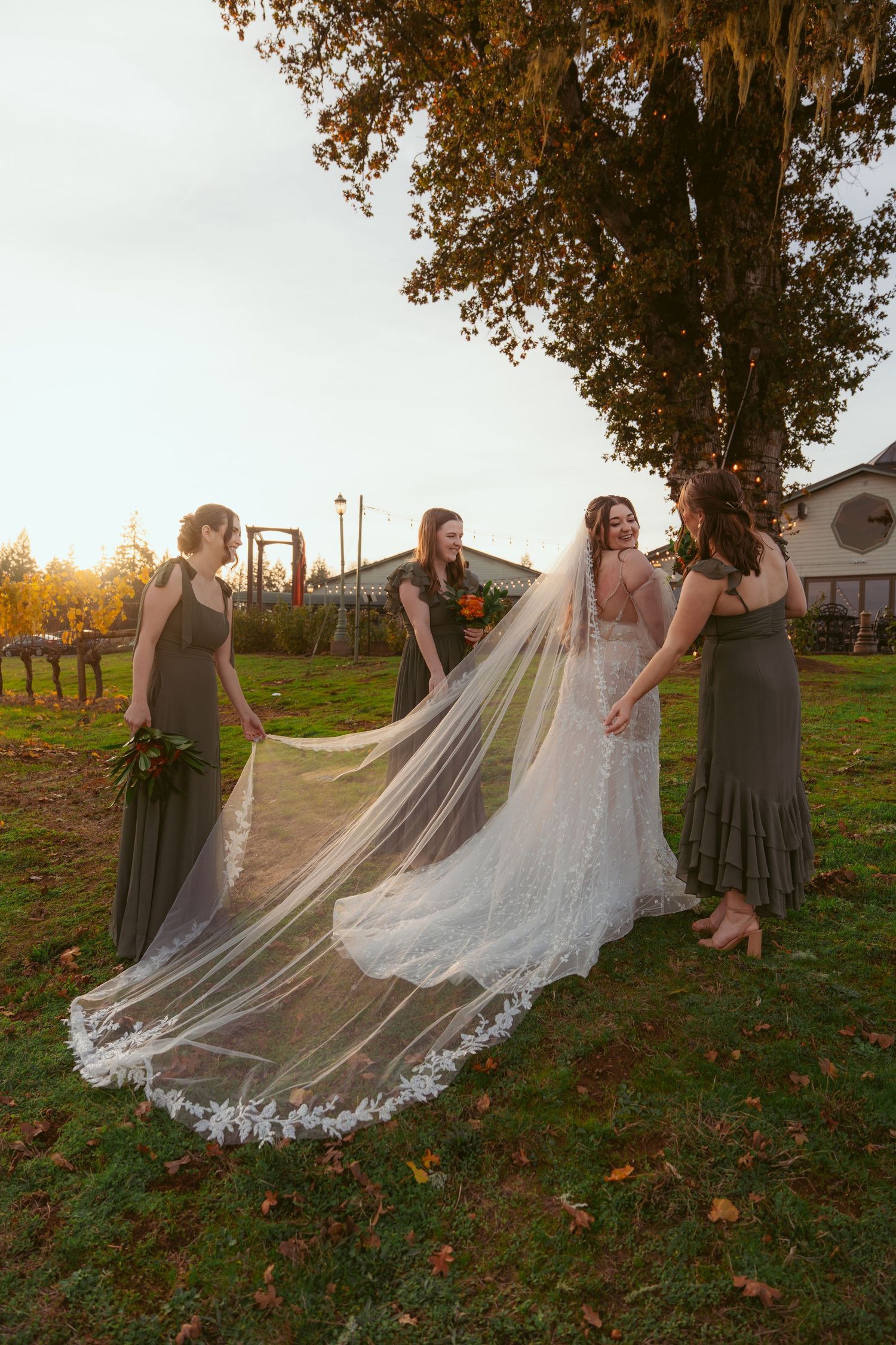 Bridal party arranges long veil during sunset photo session near vineyard.