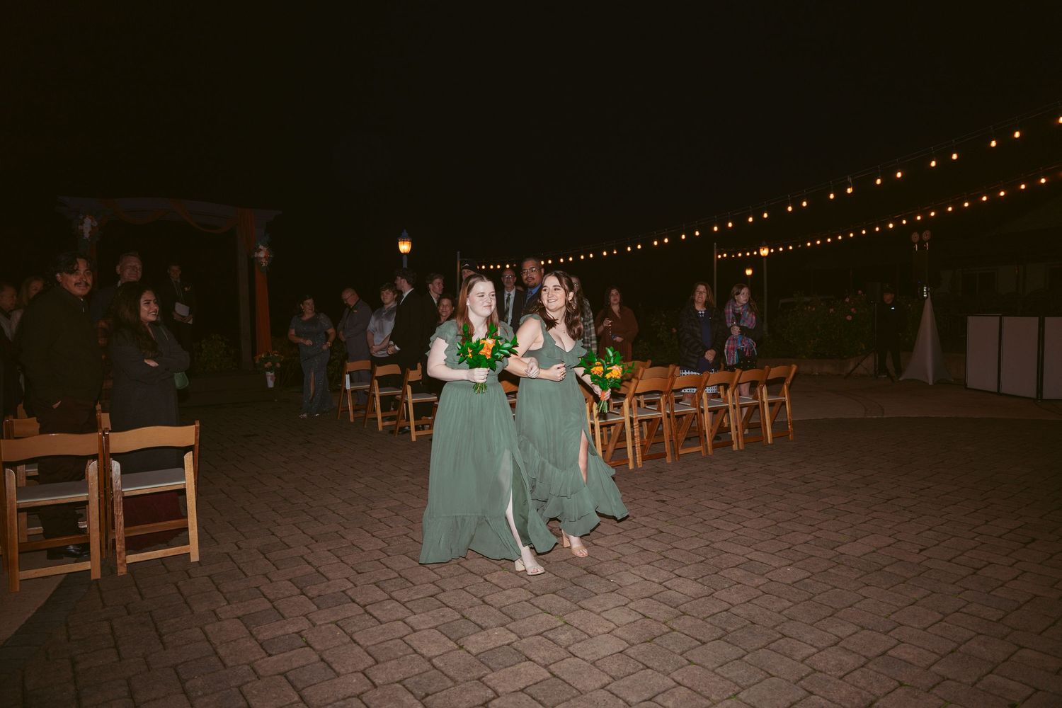 Wedding venue at night with string lights and wooden chairs arranged outdoors on stone patio.
