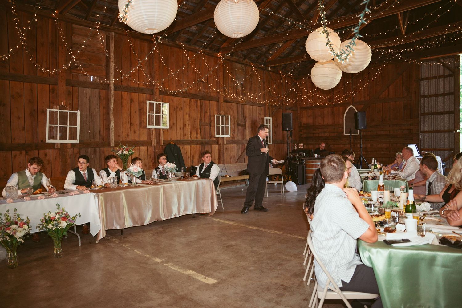 Long banquet tables arranged in a rustic barn setting with elegant lighting.