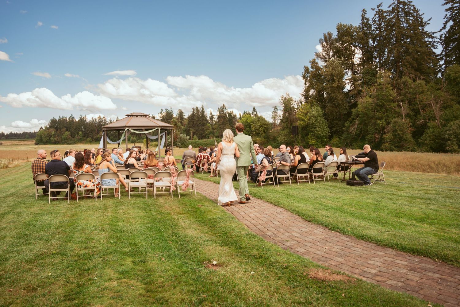 Outdoor wedding ceremony setup with chairs on grass and brick pathway leading to wooden arch.
